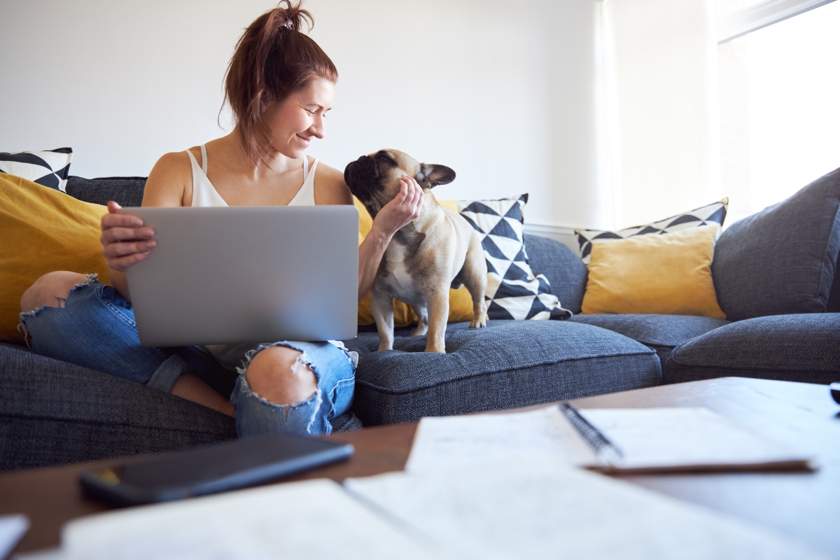 A woman using a laptop while her dog sits with her